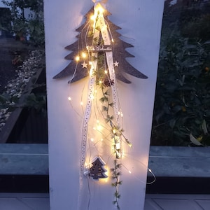 Könnte beinhalten: Graue Weihnachtsbaumdekoration aus Filz mit weißem Stern, Lichterkette und weißem Band mit "Frohe Weihnachten". Sie hat einen kleinen Holzbaum und künstliches Grün. Die Dekoration ist an einem weißen Pfosten befestigt.