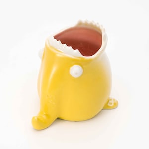 Puede incluir: Una taza de cer&aacute;mica amarilla con forma de pez con la boca abierta y un interior rojo. La taza tiene un borde blanco y un ojo blanco.