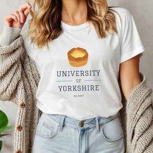 Peut inclure: T-shirt blanc avec un graphique d'un pudding du Yorkshire et le texte "University of Yorkshire" et "Be Reet".