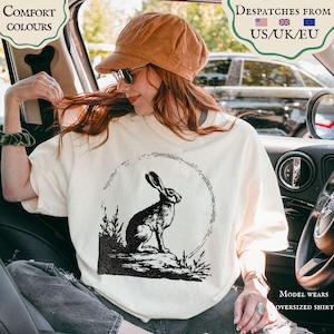 Może przedstawiać: Kremowa koszulka oversize z czarno-białą ilustracją królika w okrągłej ramie. Na koszulce widnieje napis "Comfort Colours". Modelka ma na sobie sztruksowy kapelusz i okulary przeciwsłoneczne.