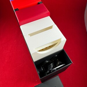 May include: A set of colorful boxes with a black box on top. The black box is open and contains a set of black rings. The boxes are stacked on top of each other and are arranged in a vertical line. The boxes are made of a hard plastic material and have a smooth finish.