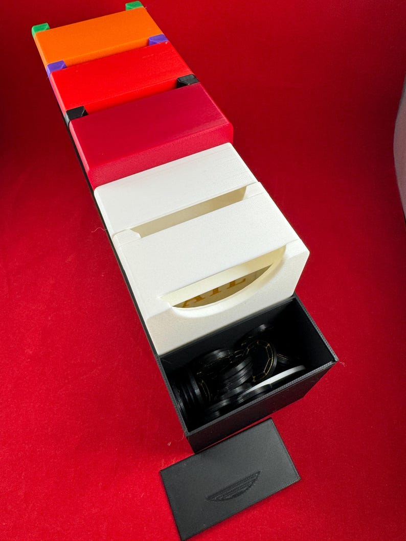 May include: A set of colorful boxes with a black box on top. The black box is open and contains a set of black rings. The boxes are stacked on top of each other and are arranged in a vertical line. The boxes are made of a hard plastic material and have a smooth finish.