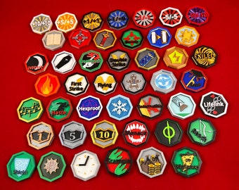 May include: A collection of 30 colorful, octagonal game tokens with various symbols and text, including "First Strike", "Flying", "Hexproof", "Haste", "Lifelink", "Exiled", "Trample", "Shield", "Night", "10/+10", "5/+5", "1/+1", "5/-5", "10/10", "1", "5", "10", and "Φ".
