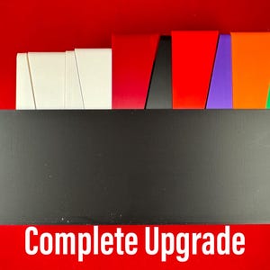 May include: A black box with the text "Complete Upgrade" on the front. The box is sitting on a red surface. There are several colored pieces of paper stacked on top of the box.