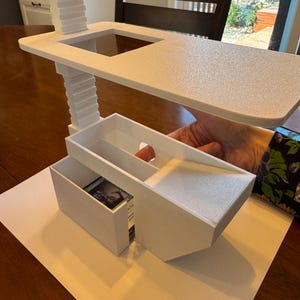 May include: White plastic organizer with a tiered shelf and a drawer. The drawer is open and contains a small card with a picture on it.