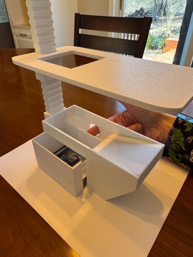 May include: White plastic organizer with a tiered shelf and a drawer. The drawer is open and contains a small card with a picture on it.