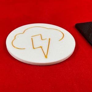 May include: A white round coaster with a gold lightning bolt inside a cloud design.
