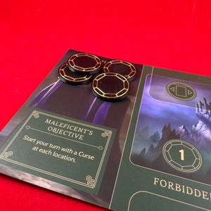 May include: A green game board with a black and gold card that reads "Maleficent's Objective: Start your turn with a Curse at each location."  There are four black and gold tokens on the board.