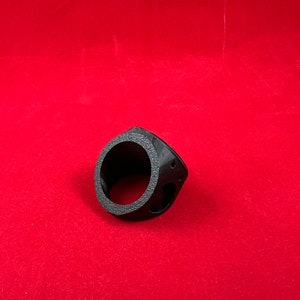 May include: A black plastic ring with a circular opening and a textured surface. The ring is designed to fit around a pipe or other cylindrical object.