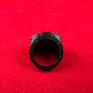 May include: A black plastic ring with a circular opening in the centre. The ring is textured and appears to be made of a 3D printed material.