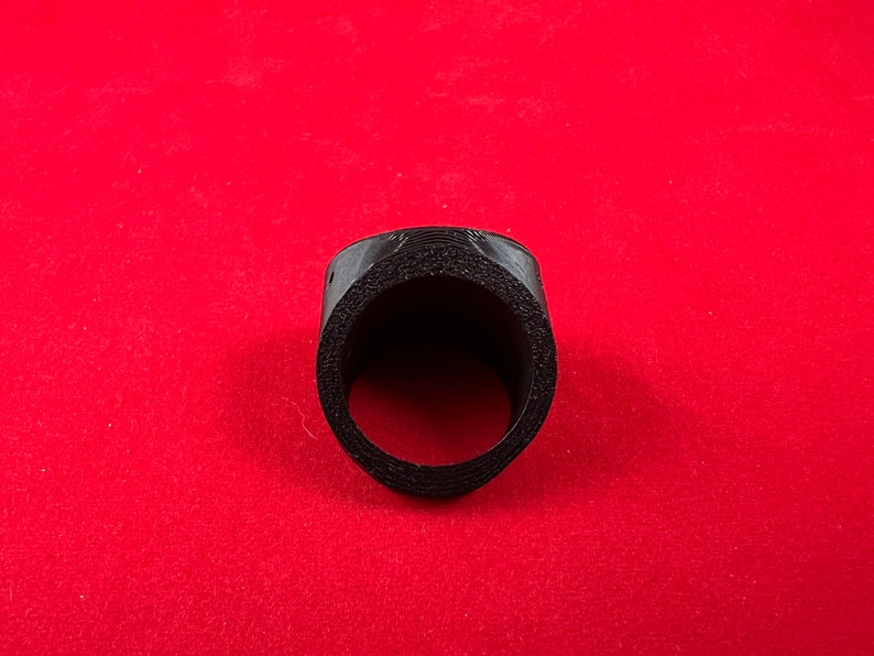 May include: A black plastic ring with a circular opening in the centre. The ring is textured and appears to be made of a 3D printed material.