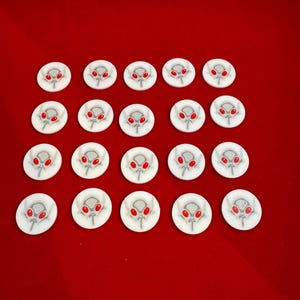 Può includere: Ventuno pedine bianche e circolari con un disegno a testa di alieno grigio e occhi rossi. I pezzi sono disposti su uno sfondo rosso pieno. Le teste aliene hanno una piccola linea verticale bianca sotto.