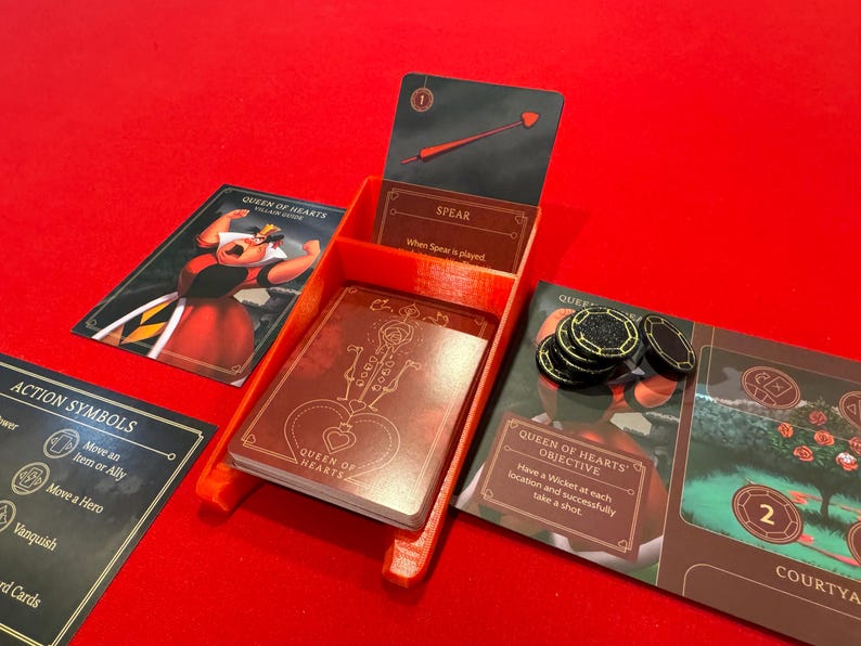 May include: A red plastic game organizer with a Queen of Hearts card, a Spear card, and a Queen of Hearts objective card. The organizer has a slot for each card and a space for tokens.