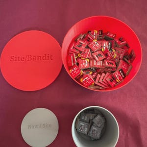 May include: A red plastic container with a lid labeled "Site/Bandit" and a separate container labeled "Naval Site." The open container holds numerous small, red game pieces. A second container holds gray game pieces. The game pieces have text.