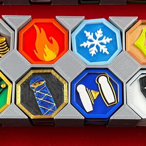 May include: A set of 12 octagonal game tokens with various symbols and colors, including a clock, musical notes, a fire, a snowflake, a coffin, and a gingerbread man. The tokens are arranged in a hexagonal pattern on a gray background.