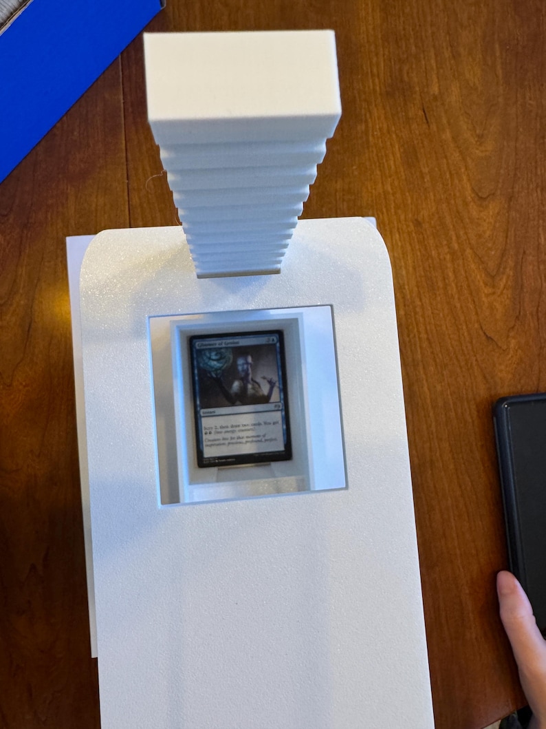 May include: A white foam display stand with a card game card inside. The card is a blue and white Magic: The Gathering card with the text "Chancellor of the Spires".