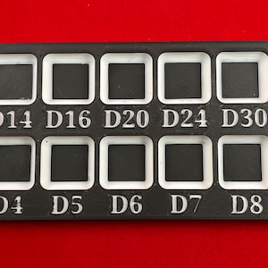 May include: A black plastic dice tray with white compartments for different dice sizes. The compartments are labeled D3, D4, D5, D6, D7, D8, D10, D12, D14, D16, D20, D24, D30, and D100.