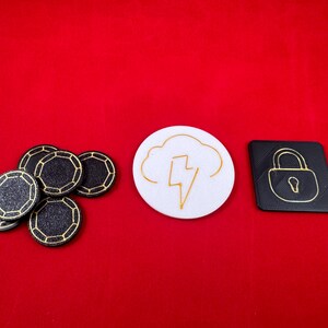 May include: A set of black and gold poker chips, a white round token with a gold lightning bolt inside a cloud, and a black square token with a gold padlock.
