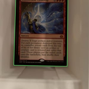 May include: A Magic: The Gathering card called "Indomitable Creativity". The card is red and blue with a white background. The card shows a person holding a blue orb with white light coming from it. The card text reads "Destroy X target artifacts and/or creatures. For each permanent destroyed this way, its controller reveals cards from the top of his or her library until an artifact or creature card is revealed and exiles that card. Those players put the exiled cards onto the battlefield, then shuffle their libraries."