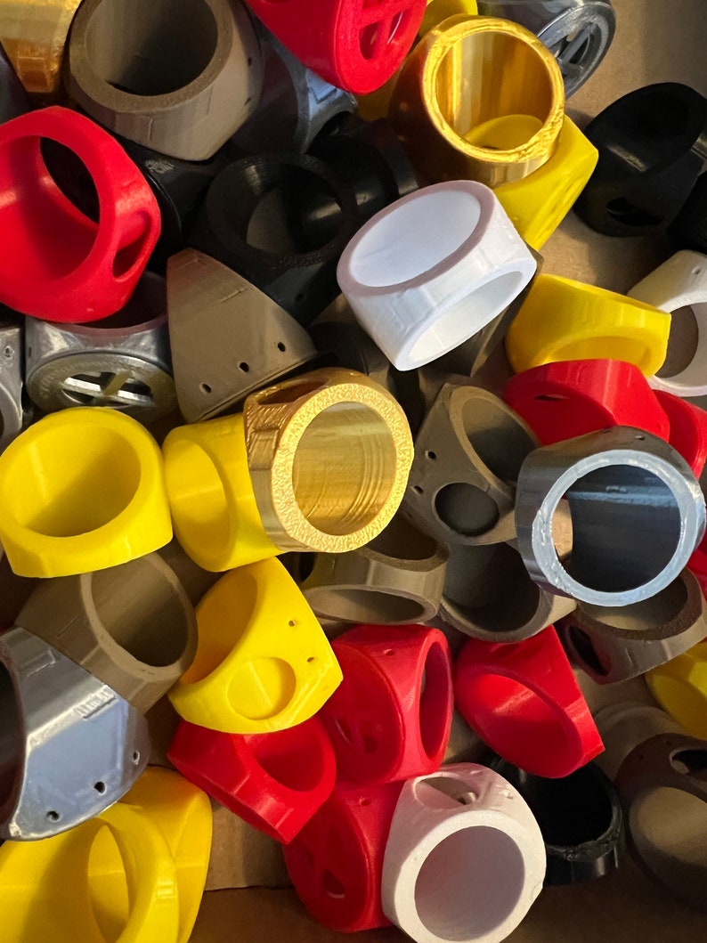 May include: A collection of colourful, 3D printed rings in various shapes and sizes. The rings are made of plastic and have a smooth, glossy finish.