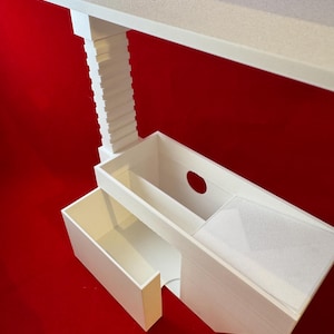May include: White 3D printed shelf unit with two drawers. The top shelf has a rectangular cutout. The unit is on a red background.