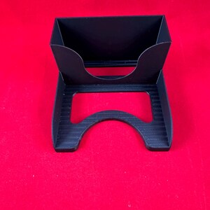 May include: A black plastic card holder with a raised lip to hold cards upright. The holder has a curved base to keep it stable.