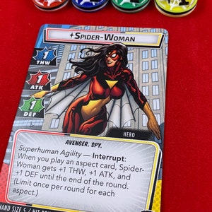 Op de afbeelding: Een Spider-Woman-verzamelkaart uit het Marvel Champions-spel. De kaart toont een illustratie van Spider-Woman in haar rood-gele kostuum met een wit spinnen-symbool op haar borst. De tekst op de kaart luidt "Superhuman Agility - Interrupt: When you play an aspect card, Spider-Woman gets +1 THW, +1 ATK, and +1 DEF until the end of the round. (Limit once per round for each aspect.)" De kaart heeft ook een handgrootte van 5 en 11 trefferpunten.
