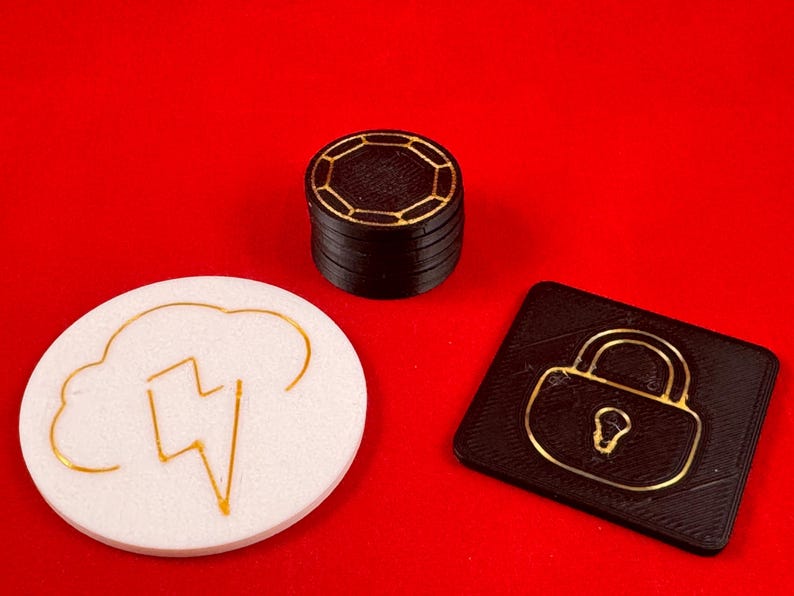 May include: Three round, black coasters with gold accents. One coaster has a cloud with a lightning bolt inside, another has a padlock with a lightbulb inside, and the third has a geometric design.
