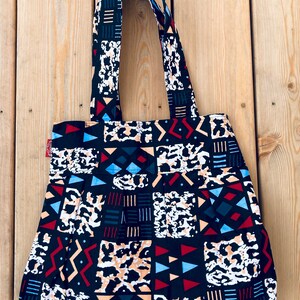Könnte beinhalten: Eine schwarze Tragetasche mit bunten geometrischen und tierischen Mustern. Die Tasche hat zwei lange Henkel.