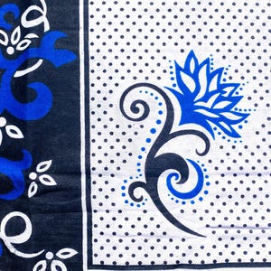 Peut inclure: Un tissu à motifs avec des motifs floraux et abstraits bleus et blancs. Le tissu a une bordure bleu foncé avec des éléments floraux blancs et bleus. Le champ principal est blanc avec de petits points noirs et un grand motif floral bleu.