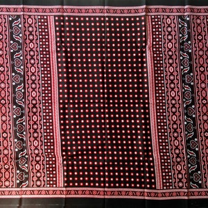 May include: Black fabric with a repeating pattern of red and white dots and geometric designs. The fabric has a traditional look.