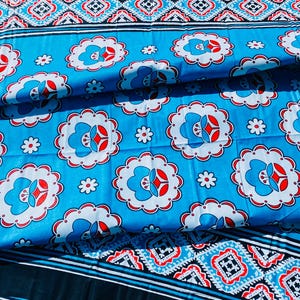 May include: A folded blue fabric with a repeating floral pattern in white and red. The fabric has a border with a geometric design in red, white, and blue. The fabric is likely a tablecloth or a similar textile.