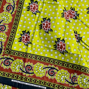 May include: A vibrant, patterned fabric featuring a repeating floral design. The fabric has a yellow background with white polka dots and is bordered by a brown and black floral pattern. Red and black flowers are scattered across the fabric.