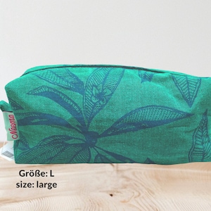 Puede incluir: Un neceser grande, rectangular, verde con un estampado de hojas azul oscuro. La bolsa tiene cierre de cremallera y una pequeña etiqueta que dice "Neema". También se ve el texto "Größe: L size: large".