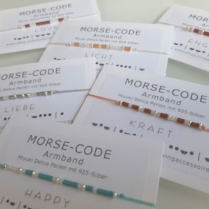 Könnte beinhalten: Sechs Armbänder mit verschiedenen farbigen Perlen und silbernen Perlen. Jedes Armband hat eine Karte mit dem Wort "MORSE-CODE" und dem Wort in Morse-Code ausgeschrieben. Die Wörter sind "LOVE", "LICHT", "ENGEL", "LIEBE", "KRAFT" und "HAPPY".