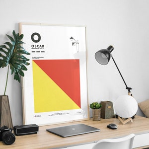 May include: A framed poster with a red and yellow diagonal design. The poster has the word "OSCAR" in black text and the words "PRONOUNCED: OSS-CAR" in smaller black text. The poster also includes a small black and white illustration of a flag.