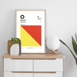 May include: A framed print of the International Maritime Signal Flag "Oscar" with a yellow and red diagonal stripe design. The flag is displayed on a white background with the letter "O" and the word "OSCAR" in black text.