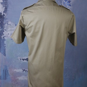 May include: A khaki short-sleeved shirt with a button-up collar and two pockets on the chest.