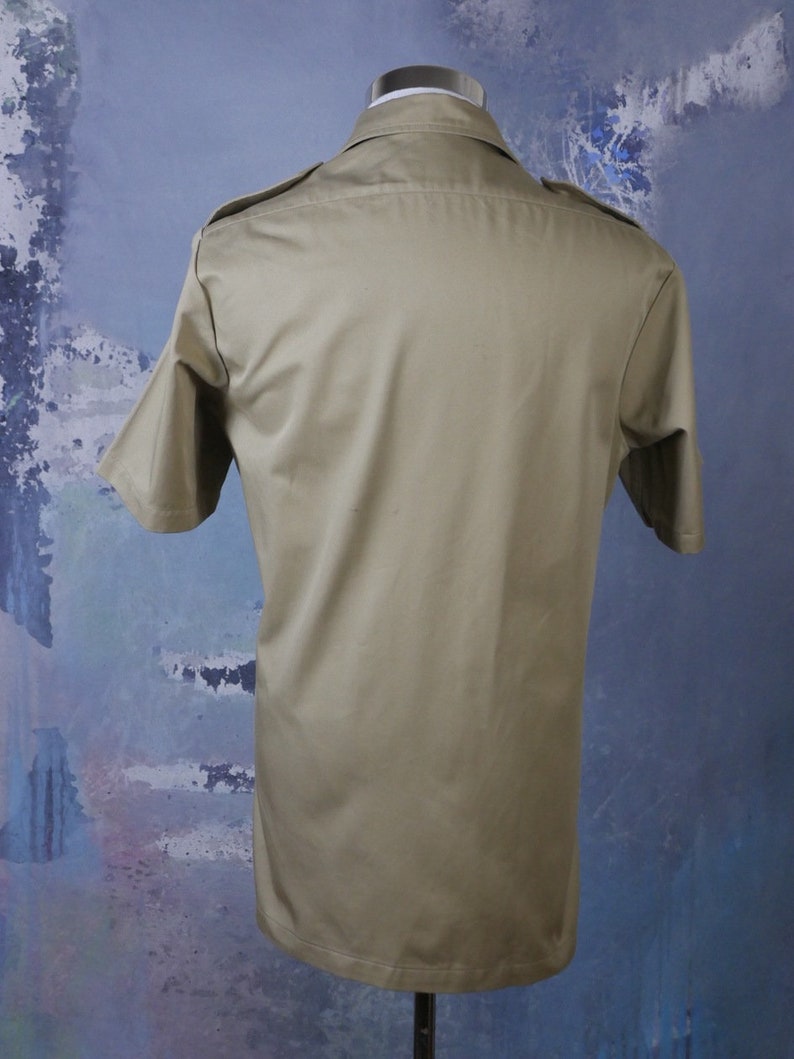 May include: A khaki short-sleeved shirt with a button-up collar and two pockets on the chest.