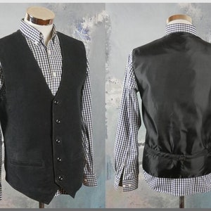 Può includere: Un gilet nero con chiusura a cinque bottoni, mostrato da davanti e da dietro. Il gilet è indossato sopra una camicia a quadri bianchi e blu. Il gilet ha uno scollo a V e una piccola tasca anteriore.