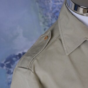 May include: A light beige long-sleeved shirt with a button on the shoulder.
