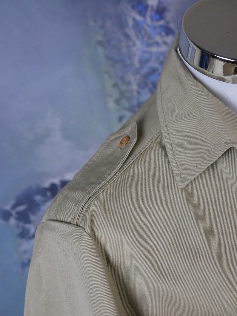 May include: A light beige long-sleeved shirt with a button on the shoulder.