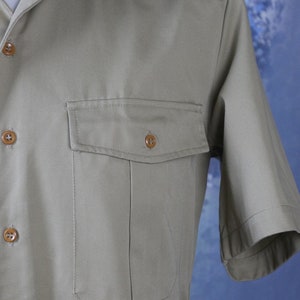 May include: A light brown short-sleeved shirt with a button-up front and a single chest pocket.