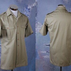 May include: A khaki short-sleeved button-down shirt with two flap pockets on the front and a button-down collar.