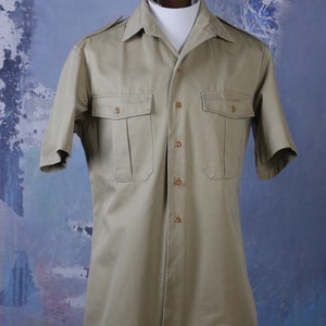 May include: A beige short-sleeved button-down shirt with two flap pockets and a pointed collar.