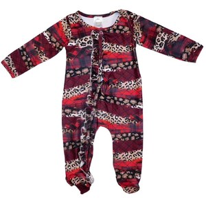 Puede incluir: Mono de bebé de manga larga rojo, negro y marrón con estampado de leopardo y cuadros. El mono tiene un frente con volantes y broches en la entrepierna.