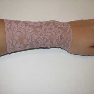 May include: A light pink lace wrist cuff with a floral pattern.