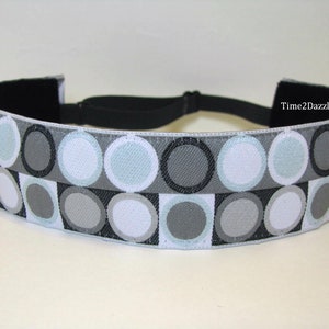 May include: A gray, white, and black headband with a geometric pattern of circles. The headband is made of fabric and has an elastic band.