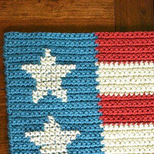 May include: A crocheted rug with a blue background and white stars. The rug has red and white stripes.
