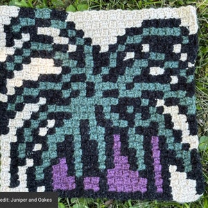 May include: A crocheted square rug with a pixelated butterfly design in black, white, green, and purple.